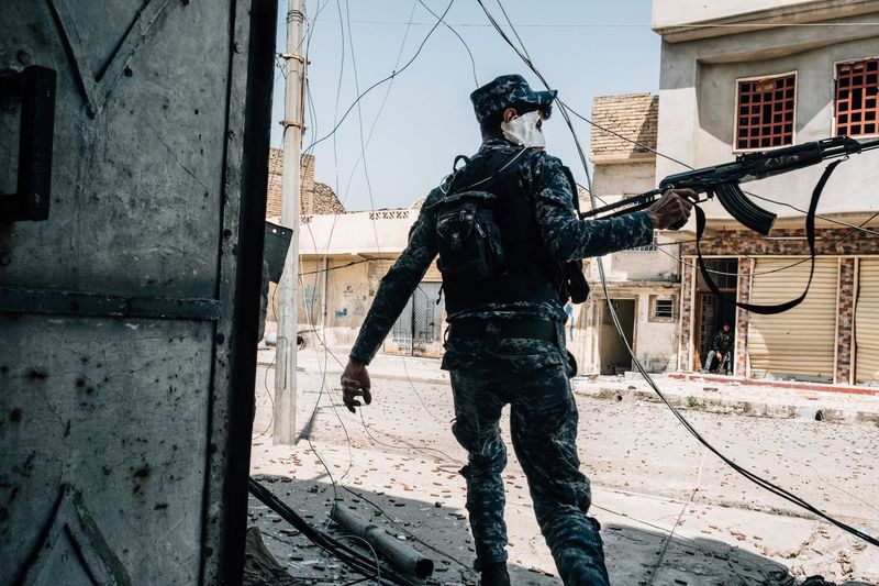 © Alexandra Howland - An Iraqi Federal Police member runs across an alley while firing his weapon towards an ISIS snipper position for cover.