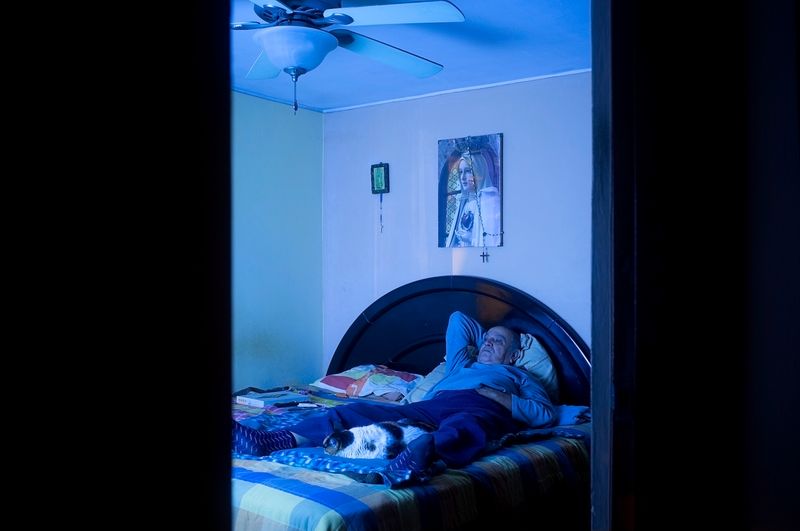 © Rochi  Leon - My dad lays in his bed with Roberta, one of his cats. He is watching his favorite show on TV, 'Pawn Stars'.