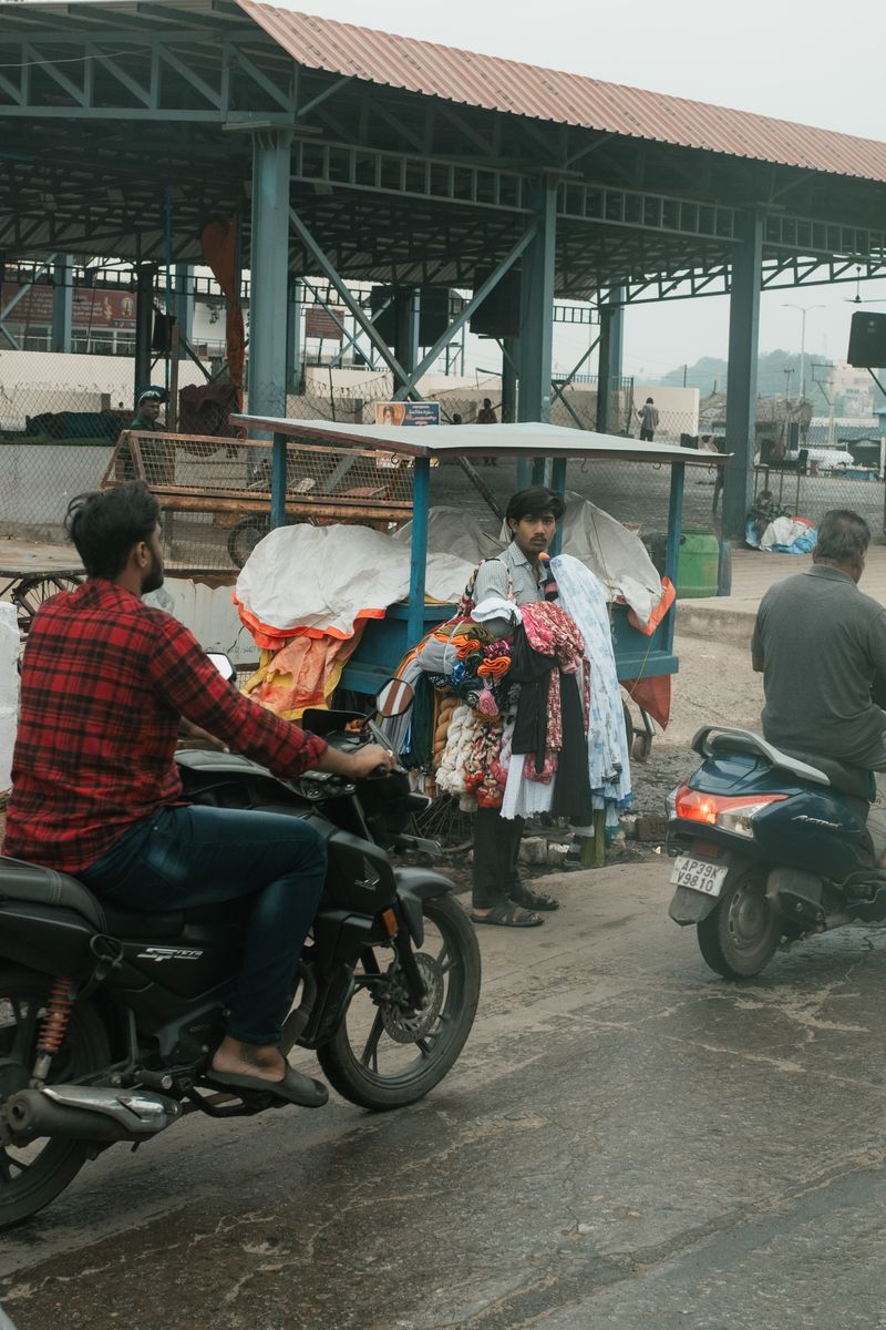 © Yvonne Chu - Street vendor at the edge of the road; commerce framed by constant passing.