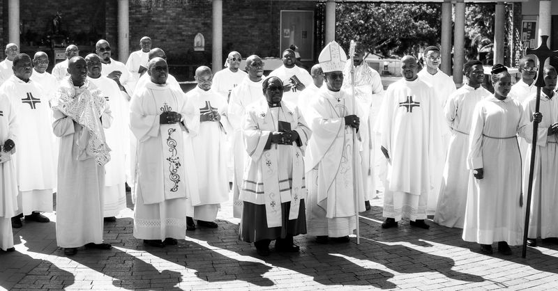 © Cole Ndelu - Priests standing in the church courtyard to receieve the congregation.
