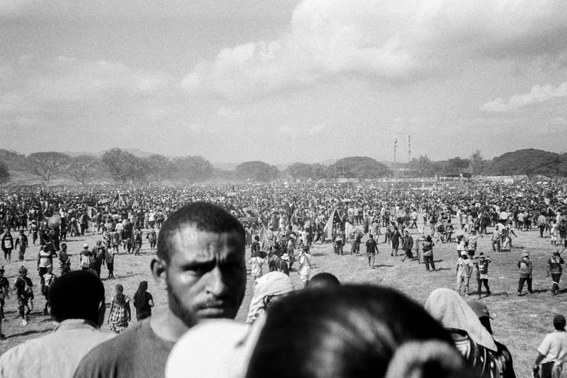 © Sean Davey - Man in crowd looking at camera (2025).