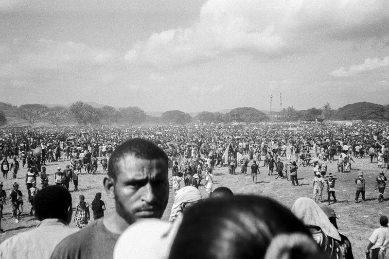 © Sean Davey - Man in crowd looking at camera (2025).