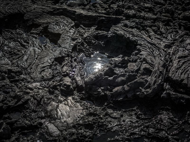 © Ilan Rabchinskey - Caldera. A pool of water reflects the sun in a pahoehoe lava formation in the Galapagos Islands.