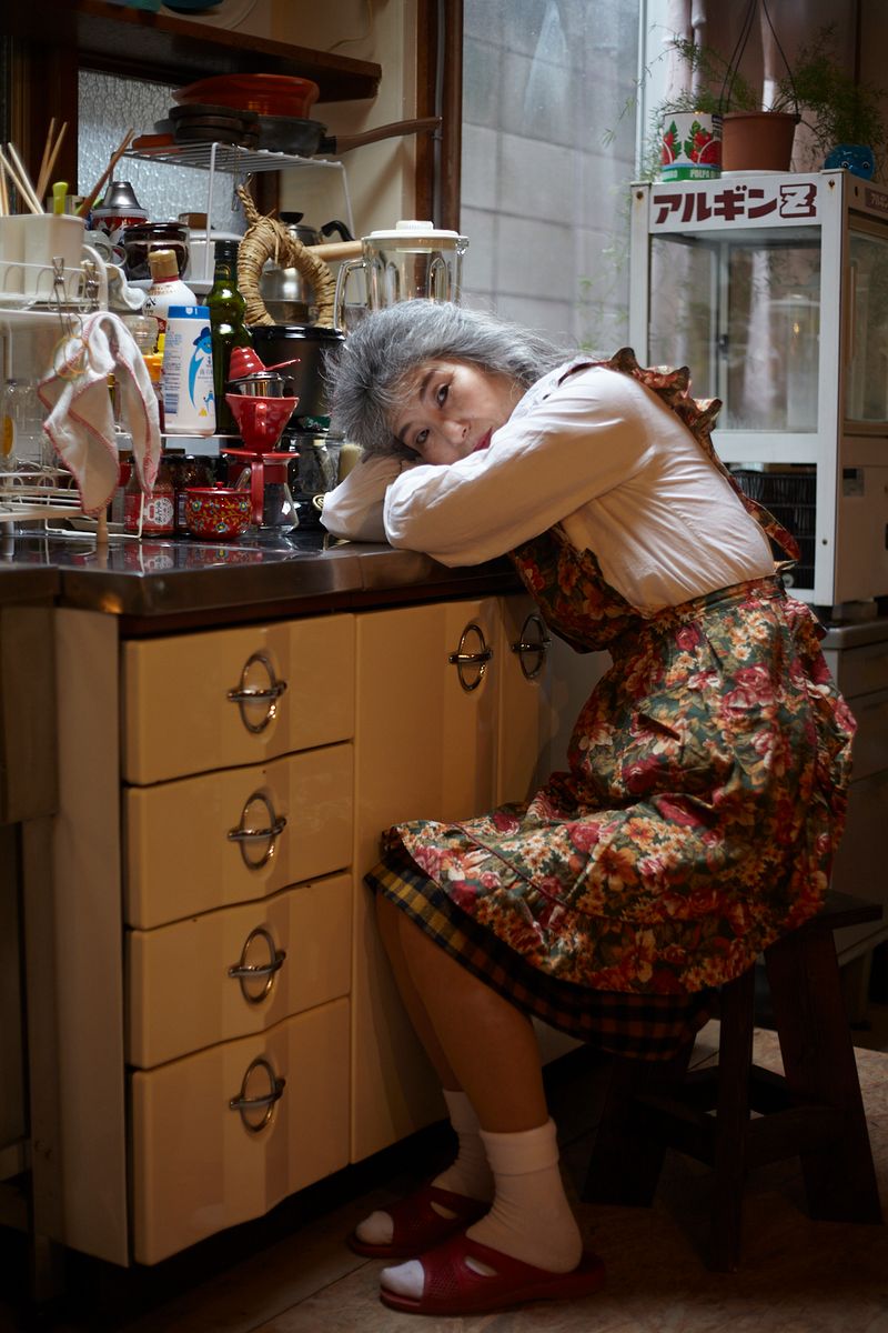 © Yuki Furusawa - Mother sitting in front of the kitchen sink, thinking about the chores she still needs to finish.