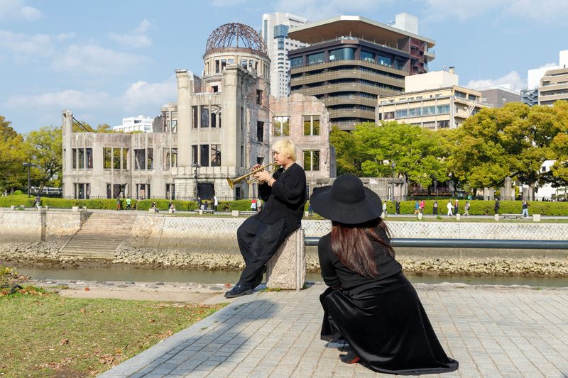 © ROBERTA LODI - "Trumpet Player in Hiroshima" A man playing trumpet in front of the Atomic Bomb Dome, memory turned sacred.