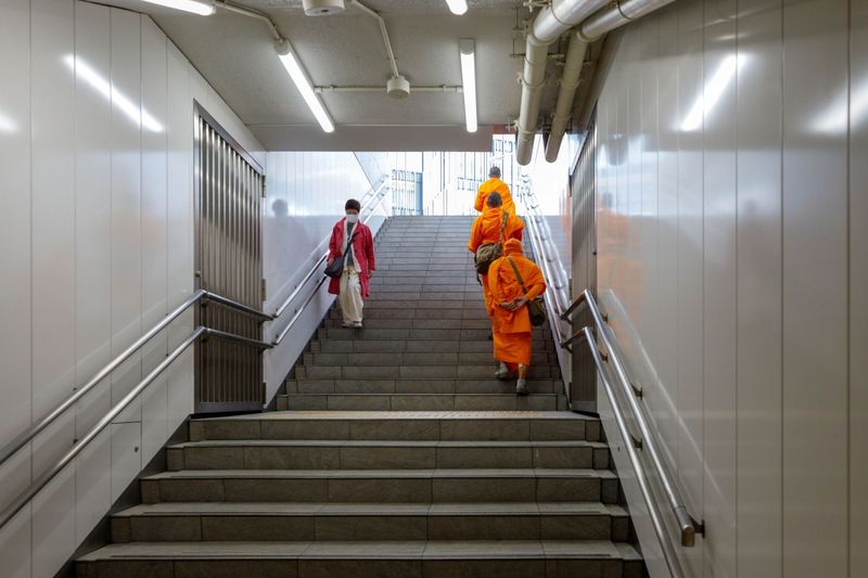 © ROBERTA LODI - "Monks in the Subway" Orange-robed monks traveling among commuters in a crowded metro carriage.