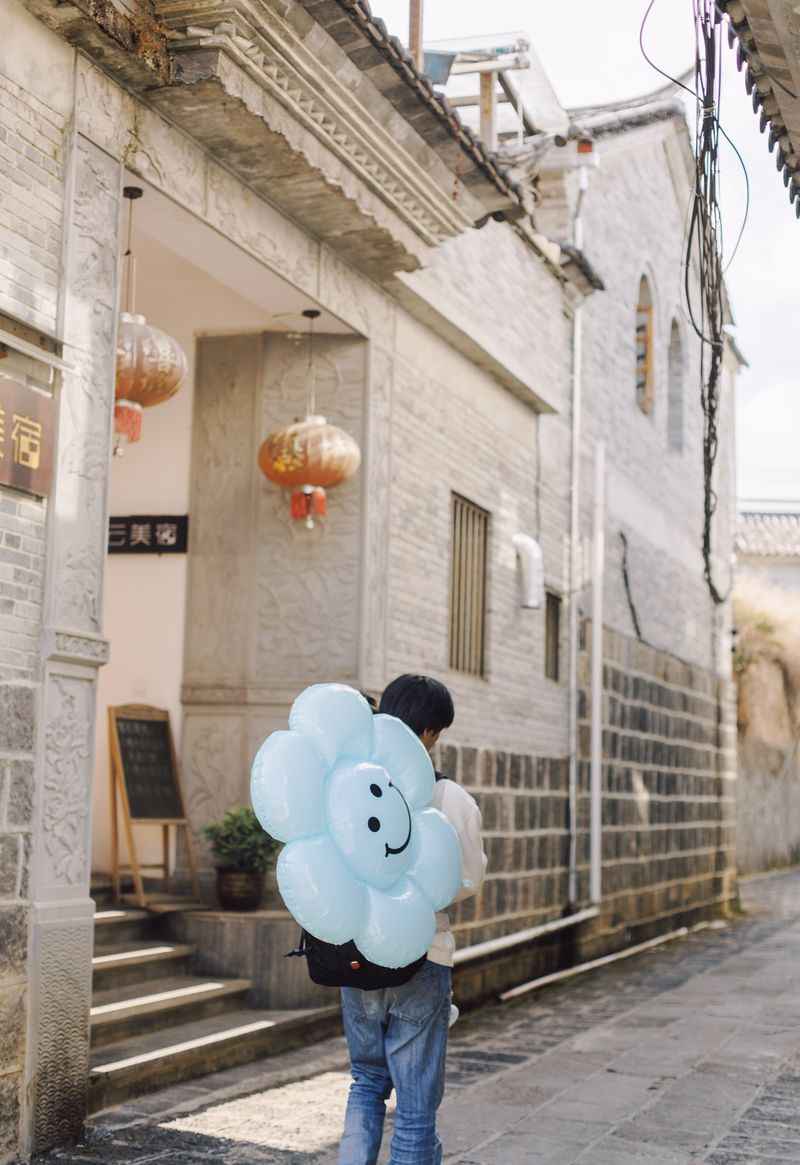 © Leafy Yun Ye - A teenager walks down the alley with a flower-shaped smiley face balloon,2022.