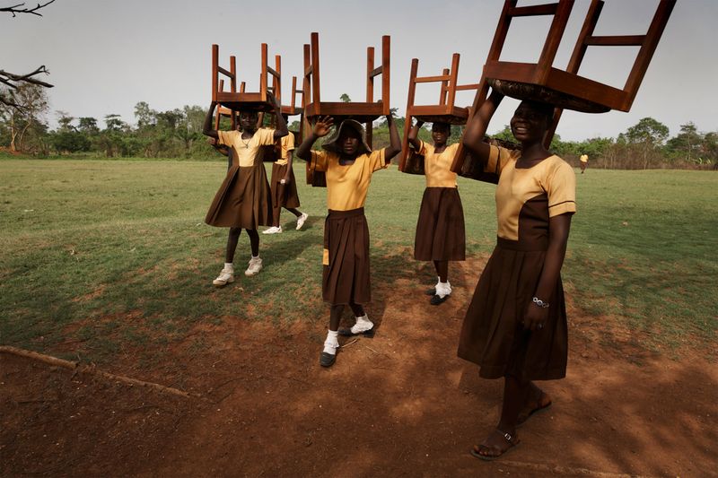 Schoolgirls in Ghana carrying chairs to the ceremony for the opening of the Maranatha Maternity Clinic