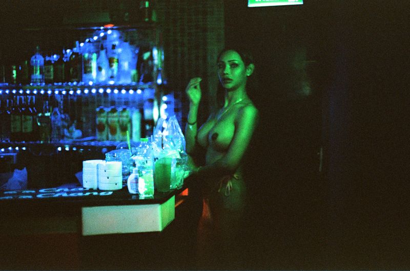 © Elizabeth Waterman - Ladyboy in green light, taking a break from work and eating a snack.