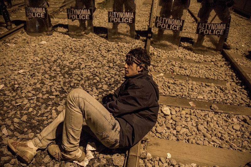 © Alessio Paduano - A man sits in front of a line of Greek police in riot gear at the Idomeni camp in Greece on March 21, 2016.