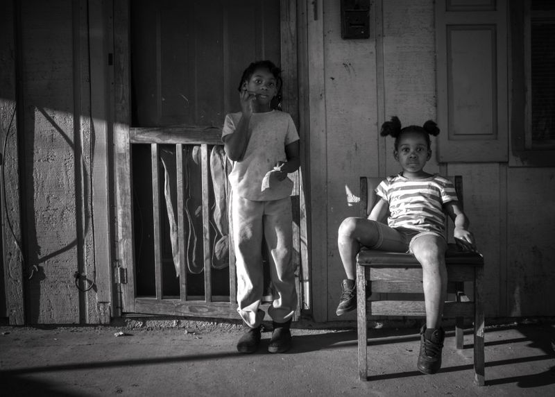 © Rebecca Moseman - Two Sisters. Two sisters play on the porch of their shotgun house in the community of Baptist Town.