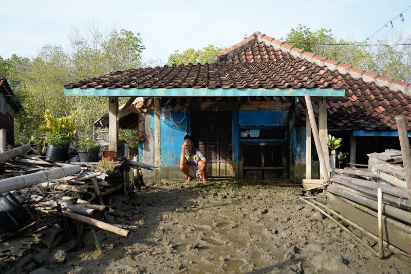 © Pakak Banak - An elderly man waits in front of his house, looking at the mud that has accumulated after the seawater flood receded