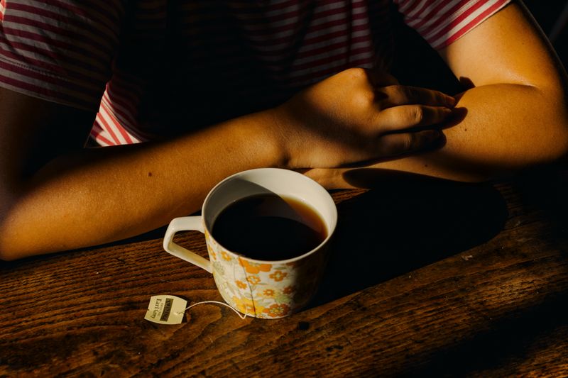© Olivia de Villaine - Parastoo's arms folded on a wooden table beside a cup of black tea. She drinks several cups a day.