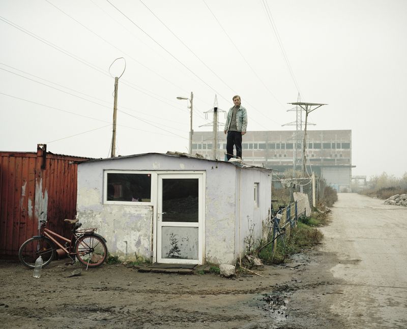 © Tommaso Rada - Romania, Giurgiu. A man working as security guard stand on a barrack in front of an abandoned factory that he watch