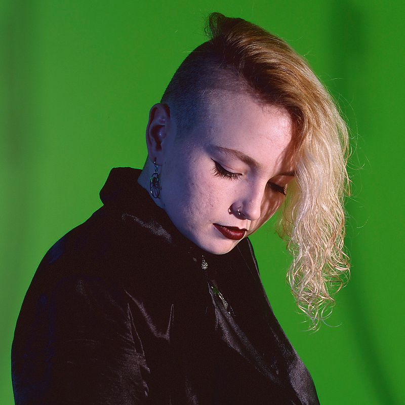 © Steven Edson - Portrait of Goth woman with partially shaved head looking away from camera.