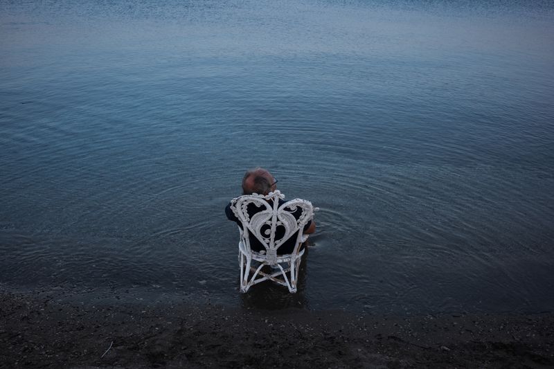 © Christopher Jones - Man in chair in waterGaritsa, Corfu.A man sits on a metal chair partially submerged in shallow water.