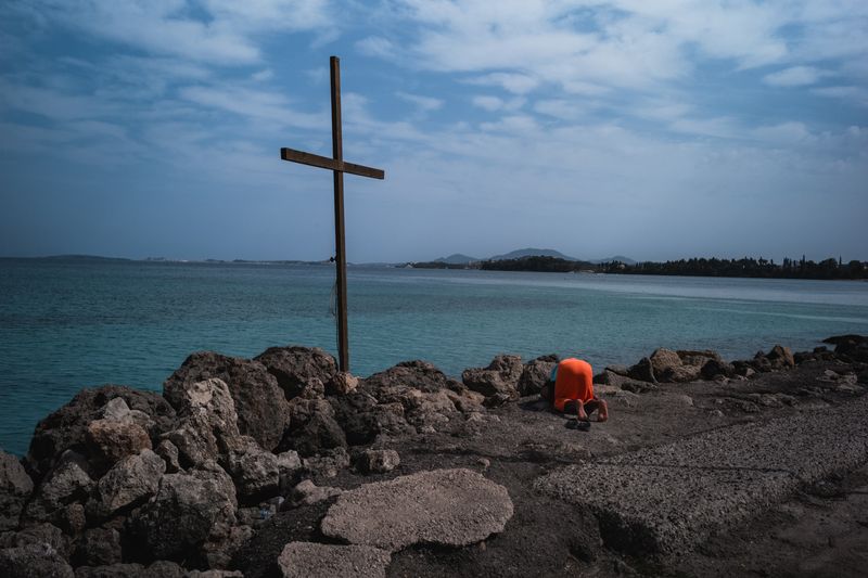 © Christopher Jones - Man praying by crossIpsos, Corfu.A man kneels in prayer beside a cross along the shoreline.