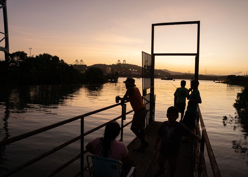 © Tova Katzman - Brown watching the sunset over the Canal as he helps a family to fish from the dock, 2022