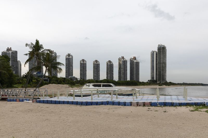 © Francesca Pompei - A rusted boat with the local logo in the beach of Forest City with abandoned skyscrapers in the background.