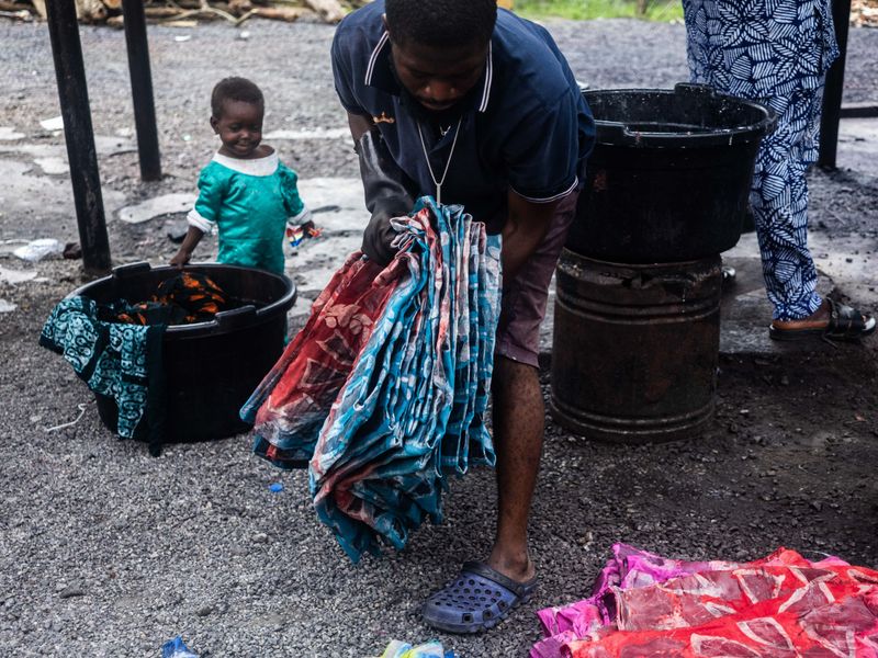 © Adegoke Kolawole - PullingA dyer lifts cloth from the dye process while a child watches nearby, Abeokuta, 2025.
