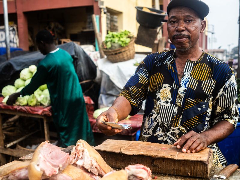 © Adegoke Kolawole - The Butcher, BodijaA meat trader holds payment at his stall while the market continues around him, Ibadan, 2025.
