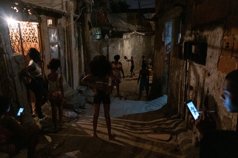 © Sabine van Wechem - The kids are playing a ballgame at night in the alley, friends are watching or they are on the mobile phone.