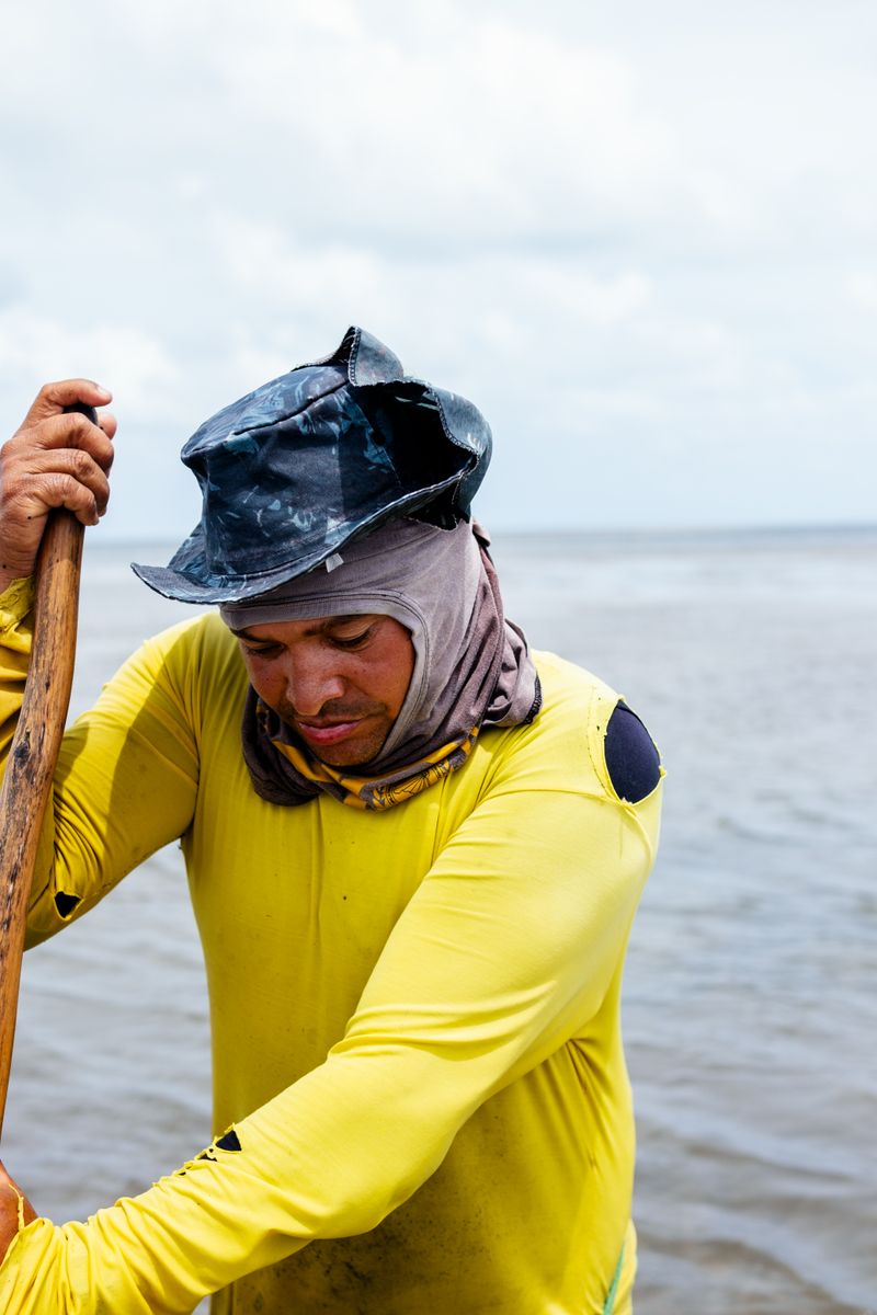 © Sabine van Wechem - A fisherman collecting small shellfish using his hands and a large net in the river that is connected to the sea.