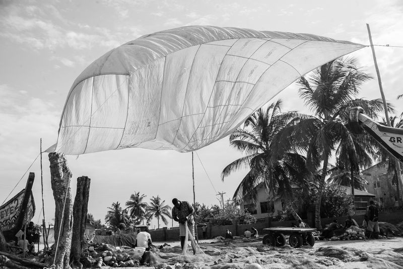 © Ofoe Amegavie - Fishermen mending fishing nets under locally manufactured Abala shed. Between Sand & Water, 2019