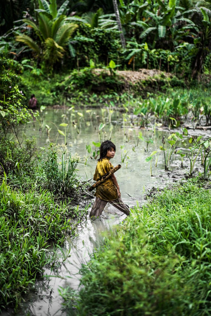 © Manolo Ty - Young Mentawain girl is looking for small fish and snails in a pond in the jungle.