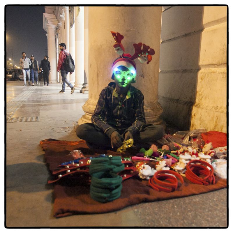© Vijay S. Jodha - Teenager wears a light mask – one of the many inexpensive items he is selling off the pavement.