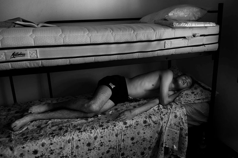 © Maria Giulia Trombini - Mark sleeps late in the morning in a shared room in the CAS house. Verona, Italy.