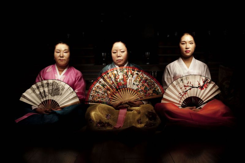 © Flore-aël SURUN - Three Mudangs (shaman women) pose with the ritual fan, on which are represented auxiliary spirits.Seoul, South Korea.