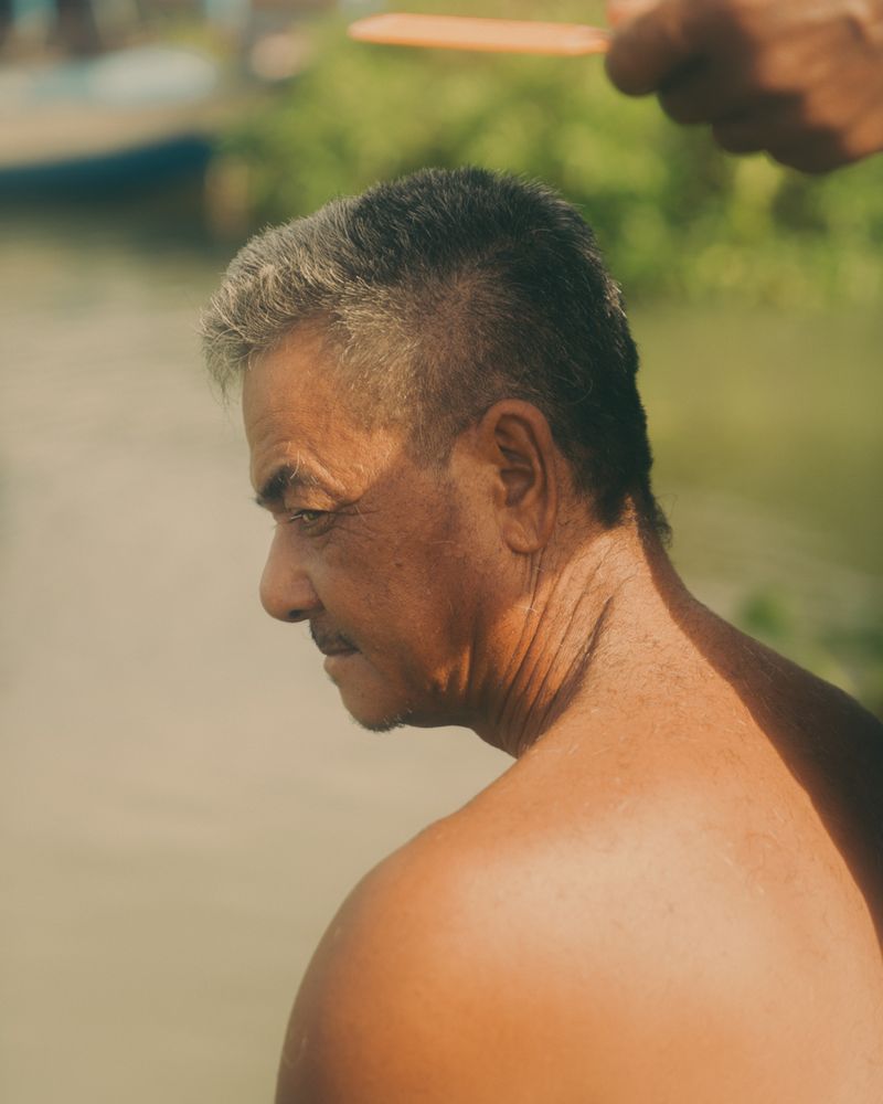 © Calvin Chow - [Untitled] Mr. Chea receiving a haircut from his nephew Mr. Cham, Phat Sanday Commune, Tonle Sap lake, Cambodia.