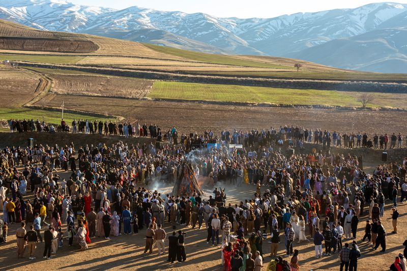 © Farbod Bavehie - A wide view of a public Nowruz gathering outdoors, with smoke rising from several fires in the distance.