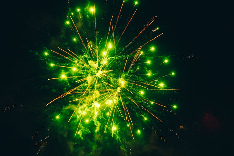 © Ryley Clarke - Green fireworks exploding against a dark night sky, with trails of yellow sparks radiating outward.