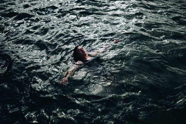 © Ryley Clarke - A person floating face-up in dark, choppy water with arms outstretched.