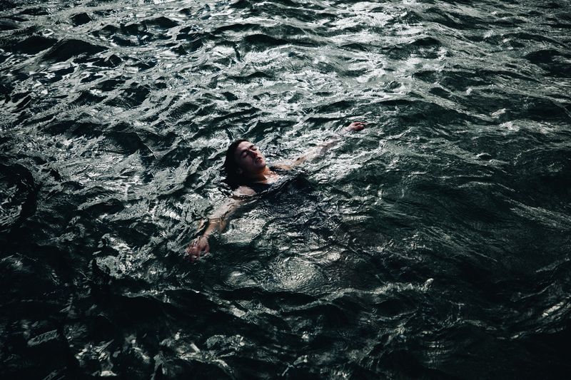 © Ryley Clarke - A person floating face-up in dark, choppy water with arms outstretched.