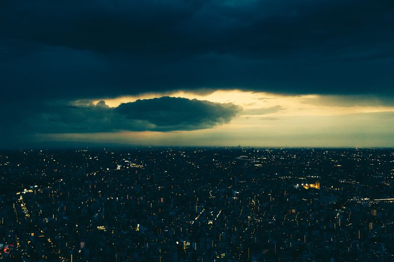 © Ryley Clarke - A cityscape at dusk under a dark, cloudy sky with city lights beginning to illuminate.