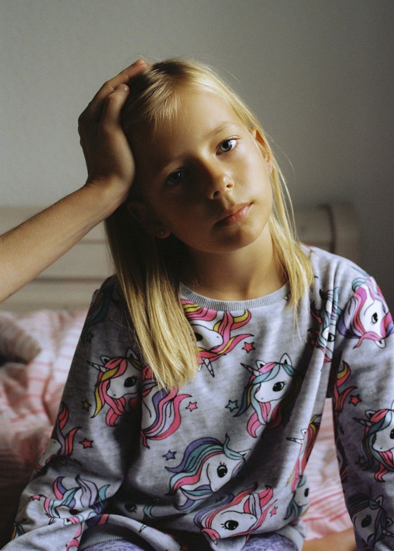 © Andrés Solla - Almut, Stefi’s older daughter, dressed in unicorn pajamas, is sitting on the bed while her mother holds her head.