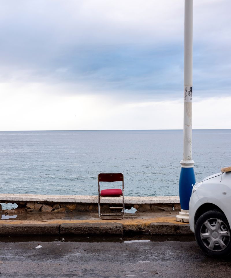 © MAryam Touzani - The horizon could be anywhere. But the chipped curb, the painted pole, the red plastic seat they tell me exactly where I am.