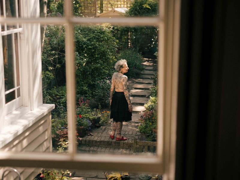 © Fotómetro - Carey in the garden, embracing the sun on her body, on a summer afternoon, seen from the window of her living room.
