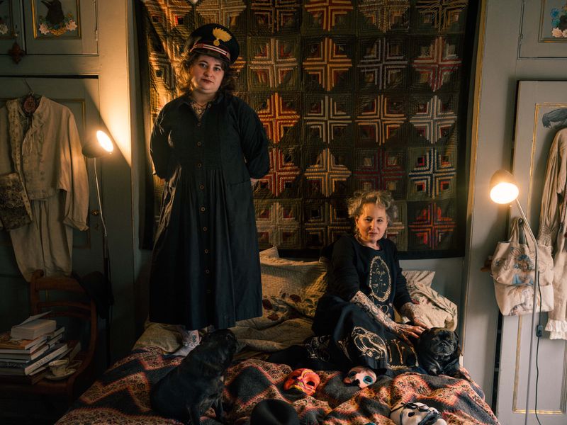 © Fotómetro - Lois standing on her mother's bed , wearing her father's hat, while Carey is petting her dogs on the bed.