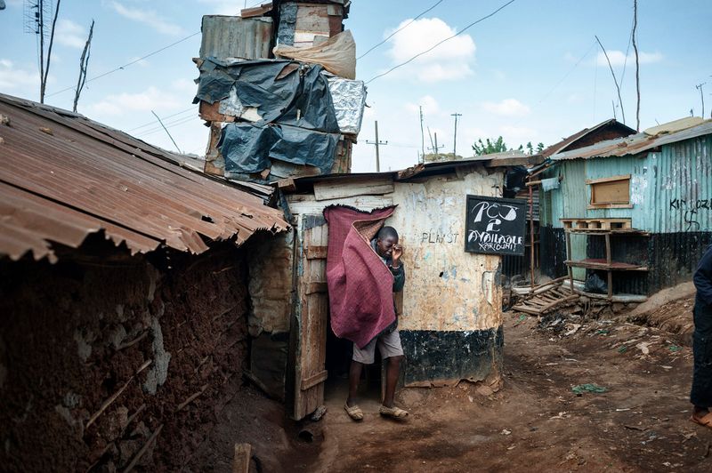 © Alessandro Grassani - Kenya, Nairobi. A boy walking out of a hut with videogames in the slum of Kibera.