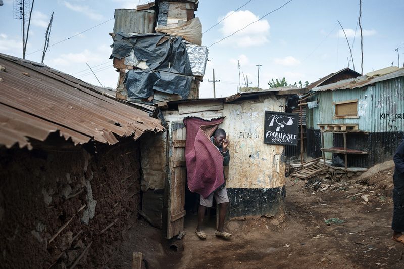 © Alessandro Grassani - Kenya, Nairobi. A boy walking out of a hut with videogames in the slum of Kibera.