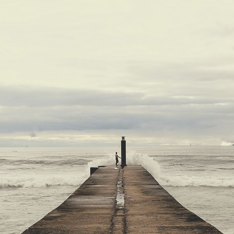© Eduardo Rosas - Surfer waiting on a narrow pier as a wave breaks beside him