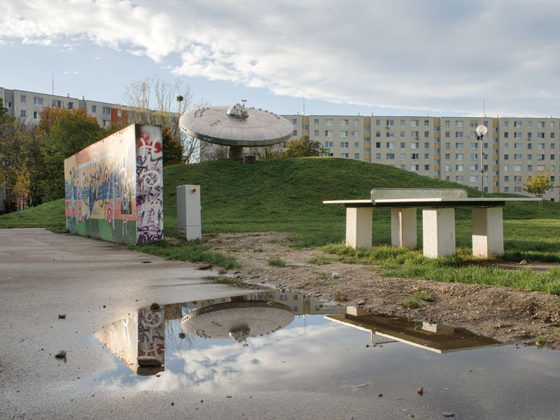 © Katerina Kouzmitcheva - The photo depicts an open urban space in Bratislava, Slovakia, featuring a distinctive UFO-like monument on a grassy mound.