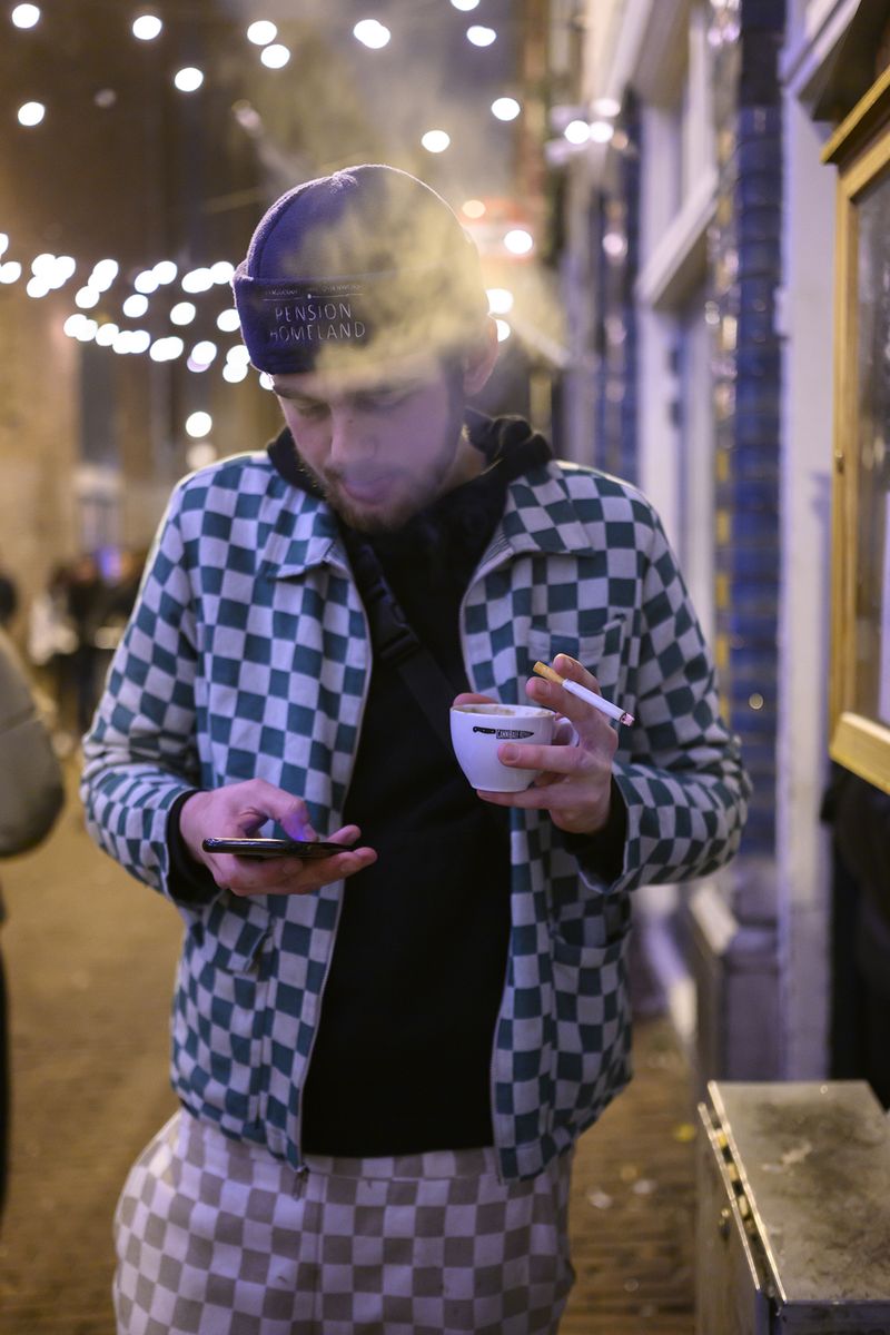 © Els Zweerink - Sammie at night in front of a club with a coffee, a cigarette and his mobile.