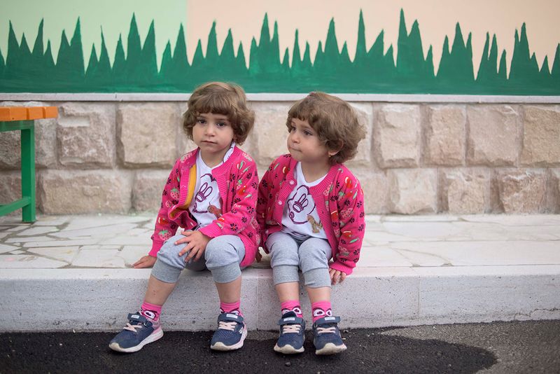© Madelaine Ekserciyan - Twin sisters waiting outside their kindergarten for their grandmother to come and pick them up.