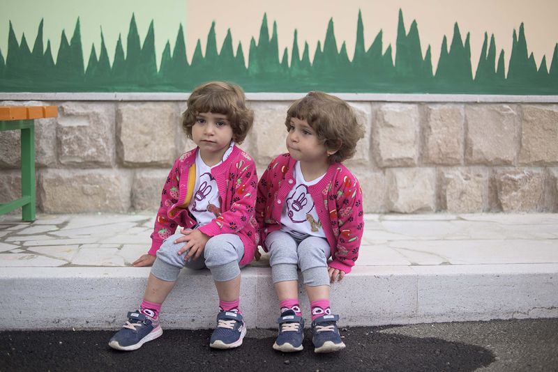 © Madelaine Ekserciyan - Twin sisters waiting outside their kindergarten for their grandmother to come and pick them up.