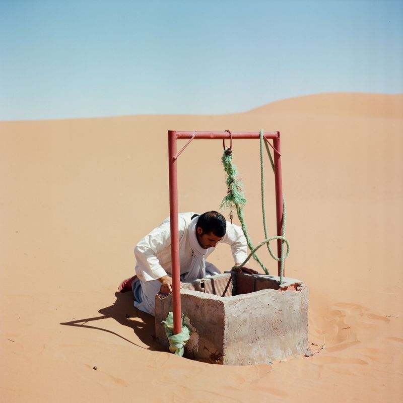 © M'hammed Kilito - A man looking for water in a well surrounded by sand dunes at the oasis of Merzouga
